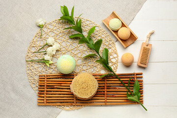 Bath bombs with massage brushes, plant branch, roses and mats on white wooden background