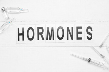 Word HORMONES with syringes and ampules on white wooden background