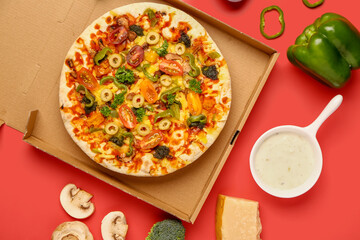 Cardboard box with vegetable pizza and ingredients on red background