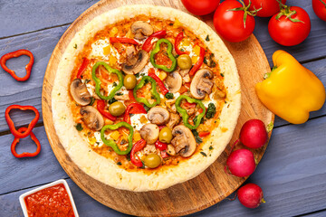 Board with vegetable pizza and ingredients on blue wooden background