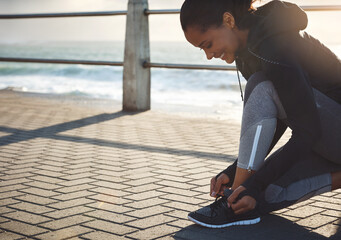 The first step is the most important. a fit young woman tying her shoelaces before going for a run on the promenade.