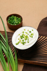 Bowl of tasty sour cream with green onion on beige background