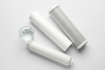 Glass of liquid and water filter cartridges on grey background