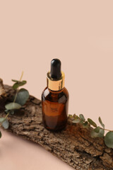 Bottle of cosmetic oil with eucalyptus branches and tree bark on pale pink background