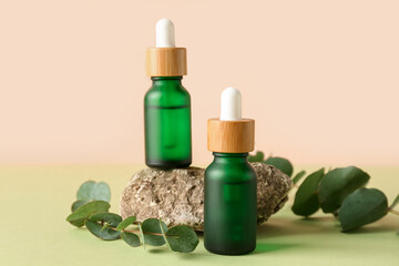 Bottles of cosmetic oil with eucalyptus branches and stone on green table