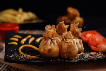 Deep fried wotons served on plate with tomatoes and sauce. fried dim sum.