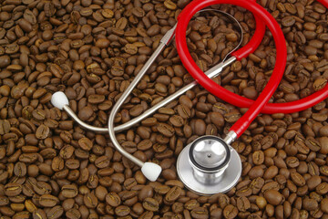 Health and coffee consumption concept. Red stethoscope on coffee beans background.