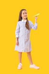 Little girl with paper plane on yellow background. Children's Day celebration
