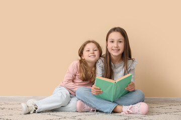 Little girls reading book near beige wall. Children's Day celebration