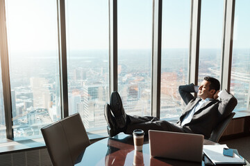 Reaping the rewards of a very successful day. a young businessman relaxing with his feet up on a table in an office.