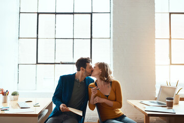 Theyre lucky they work together. young couple kissing while working together in their modern office.