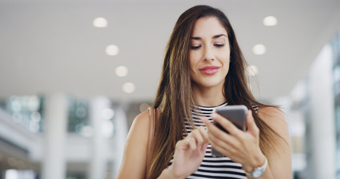 Theres no success without communication. a young businesswoman using a smartphone while walking through a modern office.