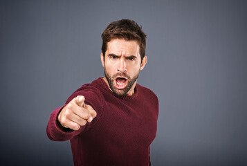 Who do you think you are. Studio shot of a handsome young man pointing a finger in anger against a...