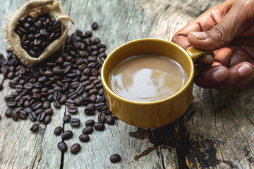 black drip coffee in ceramic cup on old wood table with coffee bean. Barista serve cup of hot black coffee on old wooden table cafe shop in garden with coffee bean.