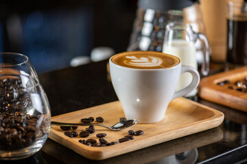White ceramic cups of cappuccino with latte art Barista make coffee by pouring spills hot milk cream on black coffee. Barista serve holding cup of hot latte and coffee beans on wooden table cafe shop