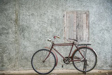 Zelfklevend Fotobehang Vintage bicycle on old rustic dirty wall house, many stain on wood wall. Classic bike old bicycle on decay brick wall retro style. Cement loft partition and window background. © worradirek