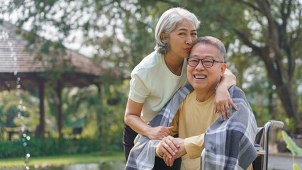 Senior woman kissing disabled husband in wheelchair with blanket while relaxation in the park