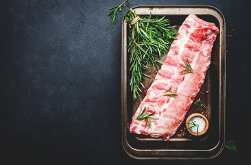 Raw pork ribs with rosemary, pepper and salt, prepared for cooking on black kitchen table...