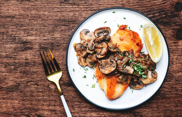 Fried chicken breast with mushrooms and onion sauce with white wine and thyme on plate, old wooden table background, top view