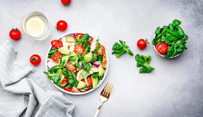 Chicken and vegetables salad with tomatoes,  avocado, cucumber, onion, lamb lettuce and sesame seeds on gray table background, top view