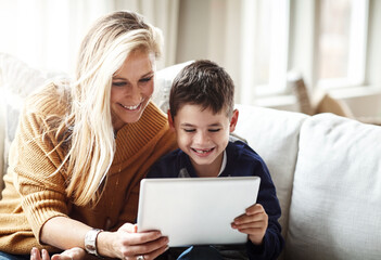 Family time in the age of the app. an adorable little boy using a digital tablet with his mother while relaxing on the sofa at home.
