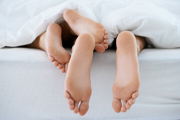 Cosy under the covers. Cropped image of a couples bare feet sticking out from under the duvet while...