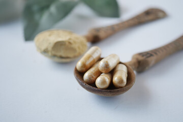 herbal medicine capsule and powder on wooden spoon on white 