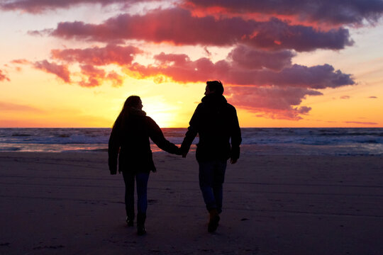 Beach, silhouette and couple holding hands at sunset while walking, bonding and enjoying freedom. Love, shadow and man with woman at the ocean for travel, romance and sunrise walk on Hawaii vacation