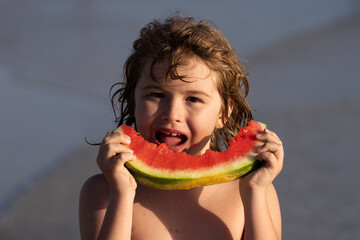 Kid eating watermelon at the beach. Child holding slice of watermelon on beach. Summer fun holiday and travel concept. Child in sea during vacation outdoors. Kid is smiling, enjoying eating fruit.