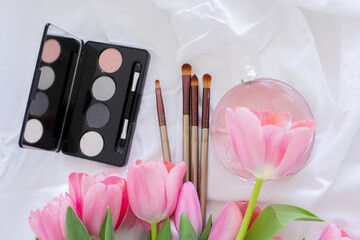 Pink tulips, eye shadow palette, brushes and perfume bottle on white background, women makeup cosmetics set