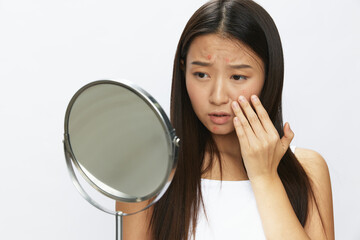 Asian woman with mirror in hand facial skin problems, acne and inflammation, red rash and...