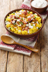 Banush or banosh is a Ukrainian dish prepared from cornmeal with cream topped with bacon, onion and bryndza closeup on the bowl on the wooden table. Vertical
