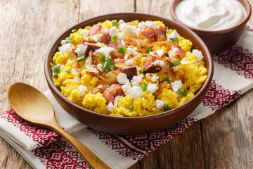 Ukrainian cuisine maize porridge with onion, cracklings and cheese closeup on the bowl on the wooden table. Horizontal