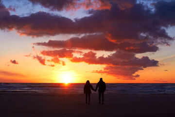 Silhouette, couple holding hands at sunset and on beach walking together. Love or care, holiday or vacation and shadows of people on the seashore for embrace for romance date or honeymoon outdoor