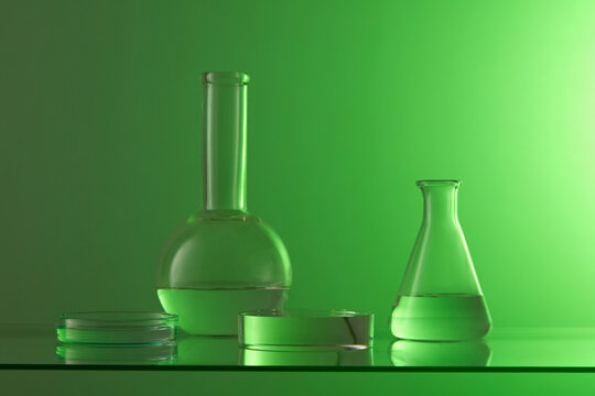 A petri dish, flat-bottom florence flask and erlenmeyer flask displayed with a round podium on a green background. Product presentation on empty podium