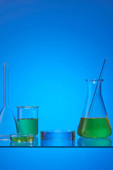 An erlenmeyer flask, petri dish and beaker filled with yellow fluid on the blue background. Empty round transparent pedestal for advertising