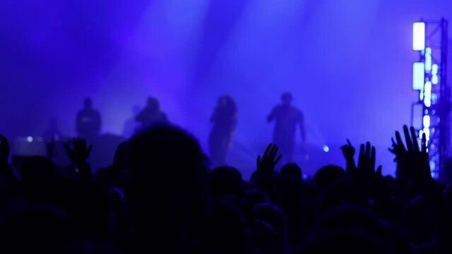 Group of Singers Performing on Stage at Live Concert with Blue Neon Lights in Front of Enthusiastic Crowd of Fans