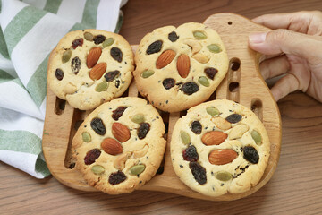 Hand Placing a Wooden Grid of Freshly Baked Almond and Raisin Cookies on the Table