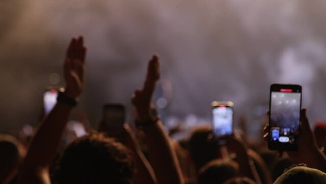 Applauding Fans recording Singer's Live Performance on Smoke-Filled and Illuminated Stage at Concert with Smartphones