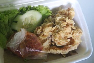 a piece of crispy chicken with sambal and vegetables on the side
