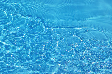 Blue water with ripples on the surface. Defocus blurred transparent blue colored clear calm water surface texture with splashes and bubbles. Water waves with shining pattern texture background.