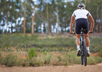 Exploring nature from the saddle. Rear view of a cyclist riding on an off-road track.