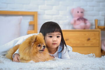 The little girl snuggled up to her furry dog friend feeling safe and content on the cozy bed in the bedroom.