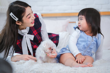 Beautiful asian woman and little girl they looked at each other with smiles as there was a little white puppy on the bed in the bedroom.