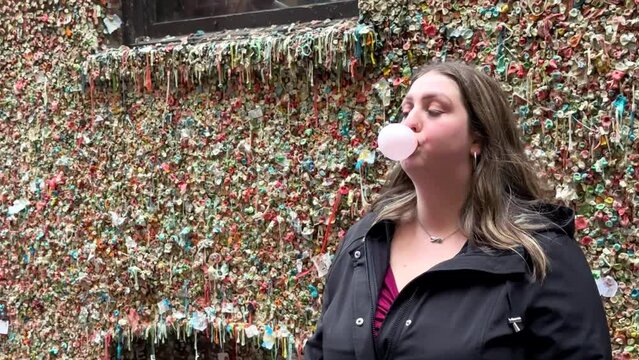 Woman Blowing Bubble Gum Ball Beside Colourful Gum Wall Under Pike Place Market In Downtown Seattle