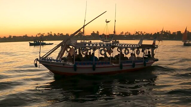 River scape of Tourists sitting on egyption Local felucca tour boats on Nile river Crossing from west to east bank with sunset colors reflecting on water. Luxor, Egypt