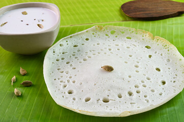 Appam breakfast served with coconut milk on a banana leaf.