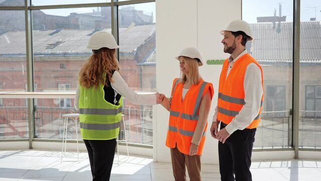 Happy young couple in protective clothing and helmets shake hands with a real estate agent after signing a contract to buy, sell, or rent a new space for a restaurant or office business.
