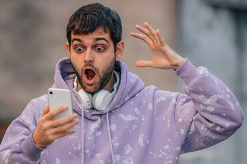 young man looking surprised at mobile phone in the street