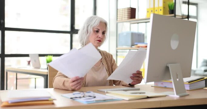 Mature business woman works on a computer and studies financial documents. Senior business seo woman holding resume and conducting job interview with remote job seeker